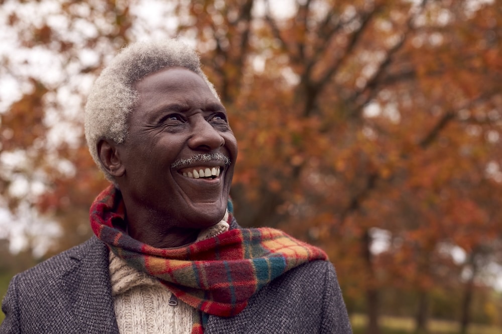 Man outside in autumn with scarf enjoying his Senior living community and fall leaves
